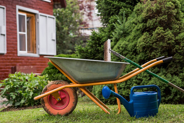 A garden wheelbarrow, rake, and watering can in the backyard of a house. The concept of gardening...