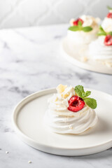 Meringues mini pavlova cake with whipped cream, fresh cherry and mint leaves on a plate, white marble background. Light summer dessert, copy space