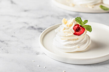 Meringues mini pavlova cake with whipped cream, fresh cherry and mint leaves on a plate, white marble background. Light summer dessert, text space