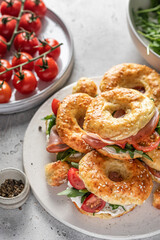 Homemade bagle sandwiches with ham, soft cheese and vegetables on whire board on kitchen table background. Homemade burgers