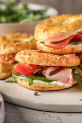 Homemade bagle sandwiches with ham, soft cheese and vegetables close up on whire board on kitchen table background. Homemade burgers