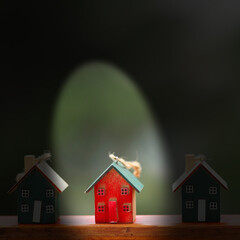 Red wooden house ornament illuminated in spotlight between two dark green ones, symbolizing...