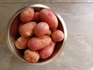 Top view of a metal bowl full of red skinned potatoes on a gray table.
