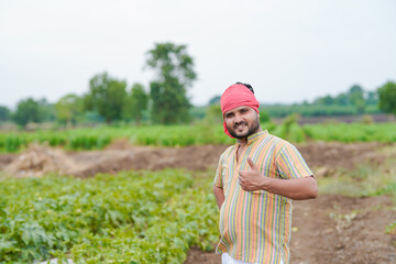 young indian farmer standing at agricultural field showing thumps up