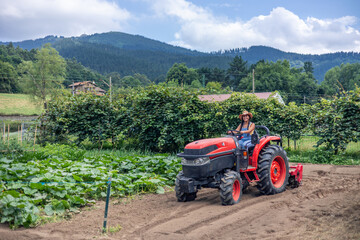Latin farmer woman driving tractor plowing field on sunny day
