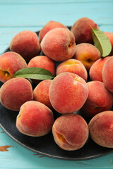 Sweet peaches and leaves on dark plate on blue wooden background. Vertical photo