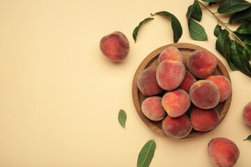 Sweet peaches and leaves on wooden plate on beige background. Space for text