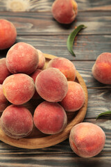 Sweet peaches and leaves on wooden plate on brown background. Vertical photo