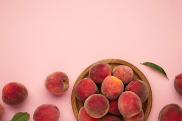 Sweet peaches and leaves on wooden plate on pink background. Space for text