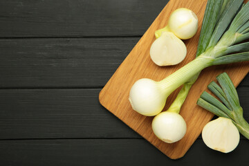 Green onion on cutting board on black wooden background.