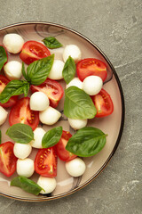 Italian Caprese salad with cherry tomatoes, mozzarella, basil on plate on grey concrete background. Vertical photo