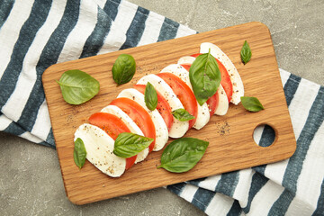 Mozzarella cheese with green basil leaves and tomato on cutting board on grey background