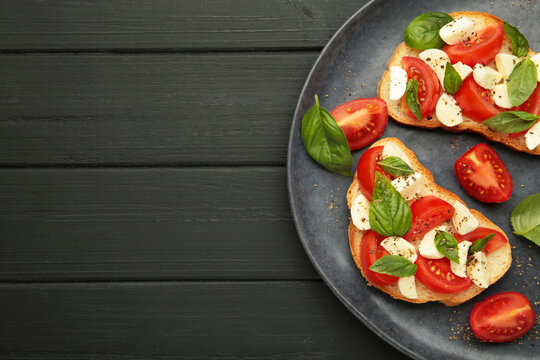 Tasty sandwich with mozzarella cheese, tomatoes and basil on dark plate on black wooden background. Caprese