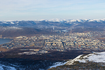 Top view of the city of Magadan, located on the seashore among the mountains. City blocks, streets and buildings. Snow-capped mountains in the distance. Beautiful cityscape. Magadan region, Russia.