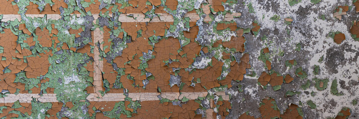 Peeling paint on the wall. Panorama of a concrete wall with old cracked flaking paint. Weathered rough painted surface with patterns of cracks and peeling. Wide panoramic grungy texture for background