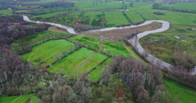 Aerial view of winding river Midden Regge in wet green fields with bare trees, nature reserve De Tatums, Hellendoorn, Overijssel, Netherlands.