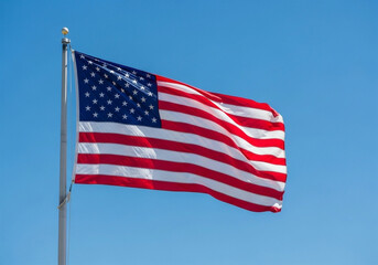 A United States flag, waving in a clear blue sky. The flag is positioned on the left side of the image copy