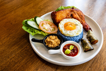 Nasi kerabu, popular delicacy in Malaysia with rice dyed in blue color, served with fried chicken, eggs, kerisik, vergetable and sambal sauces