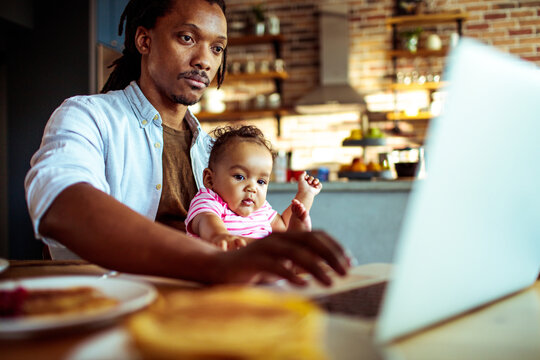 Young dad working from home while holding baby in kitchen