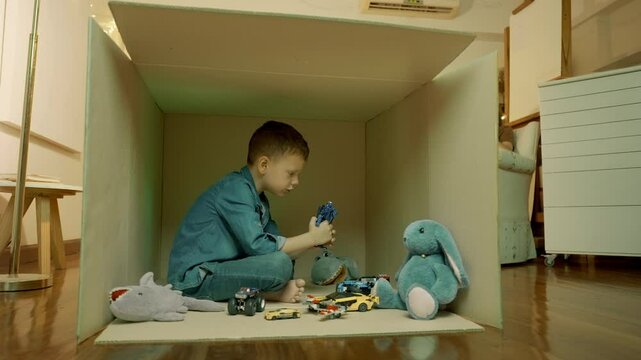 Boy with toys in cardboard box deprived of adult attention. Cardboard box as symbol of his world