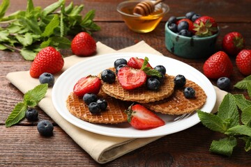 Tasty Dutch waffles (stroopwafels) with honey, berries and mint on wooden table, closeup