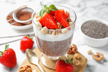 Delicious chocolate pudding with chia seeds, strawberries, yogurt and nuts in glass on white marble table, closeup