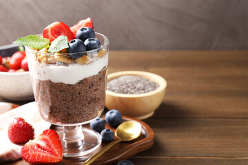 Delicious chocolate pudding with chia seeds, nuts and berries in glass on wooden table, closeup. Space for text