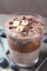 Delicious chocolate pudding with chia seeds, nuts and berries in glass on grey table, closeup