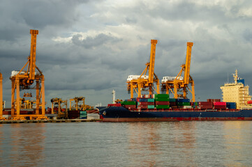 A cargo ship docked at a port, surrounded by towering cranes against a cloudy sky, showcasing...