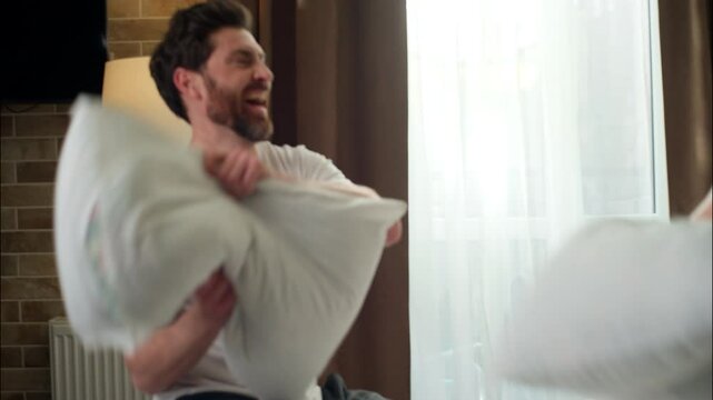 Laughing family funny Caucasian couple playing pillow battle in bedroom love married pair positive husband having fun joy wife man holding pillows woman playful fighting good morning affection humour