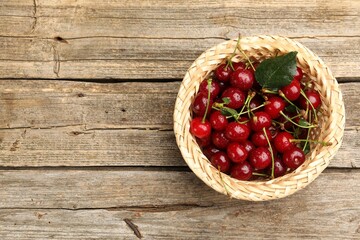 Fresh wet cherries in wicker basket on wooden table, top view. Space for text