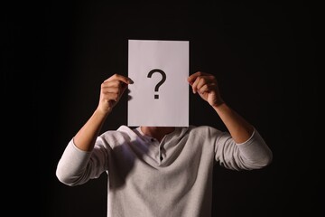 Man hiding behind paper sheet with question mark on dark background