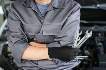 Auto parts. Professional mechanic with different wrenches near open hood of car indoors, closeup