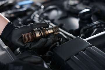 Auto part. Professional mechanic with drive shaft near open hood of car indoors, closeup