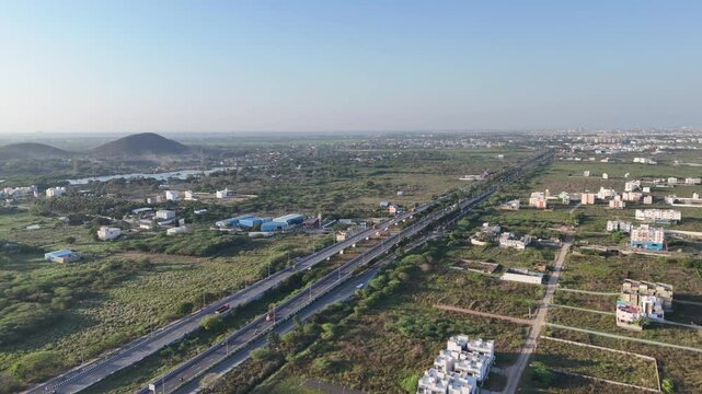 Aerial view of Chennai outskirts: multi-lane highway, scattered homes, industrial buildings, prominent lake and hills. Shows urban expansion near natural features. Plot layouts in Chennai