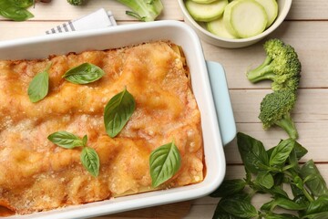 Tasty vegetarian lasagna in baking dish and ingredients on white wooden table, flat lay