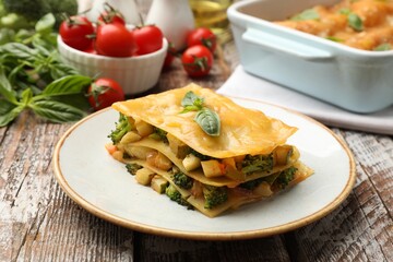 Piece of tasty vegetarian lasagna and ingredients on wooden table, closeup