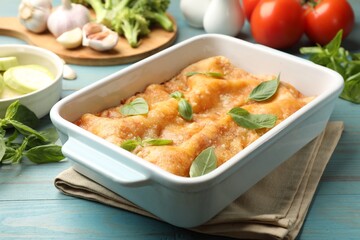 Tasty vegetarian lasagna in baking dish and ingredients on blue wooden table, closeup