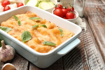 Tasty vegetarian lasagna in baking dish and ingredients on wooden table, closeup