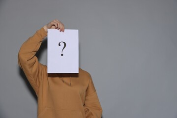 Anonymity. Woman hiding behind paper sheet with question mark on light grey background, space for...