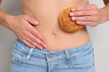 Gluten free diet. Woman with bun touching her belly on light grey background, closeup