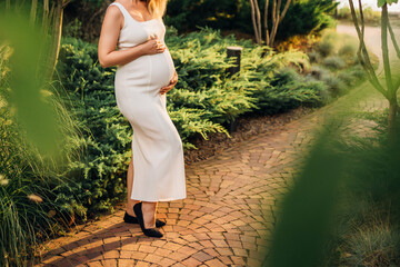 without a face. Pregnant woman in white running dress on a walk.