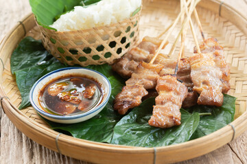 Thai style grilled pork and steamed sticky rice With Jaew dipping sauce on a wooden floor