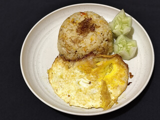 Fried rice served with sunny side up egg and fresh cucumber slices on a white plate, looks very delicious.