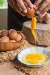 A detail of cracked egg falling into the pan as woman holds egg shells in both hands.