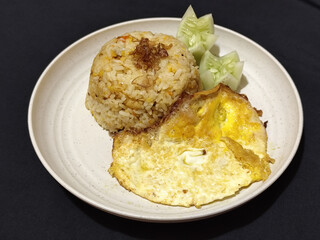 Fried rice served with sunny side up egg and fresh cucumber slices on a white plate, looks very delicious.