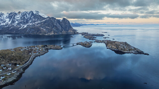 Aerial view of the bridge connecting islands in Reine, with the majestic, snow-capped mountains reflecting in the tranquil waters, Reine, Nordland, Norway. - Powered by Adobe