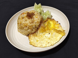Fried rice served with sunny side up egg and fresh cucumber slices on a white plate, looks very delicious.