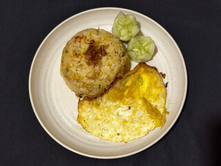 Fried rice served with sunny side up egg and fresh cucumber slices on a white plate, looks very delicious.