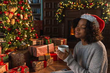 Merry Christmas. African American woman in Santa hat with cup of hot drink coffee tea near...